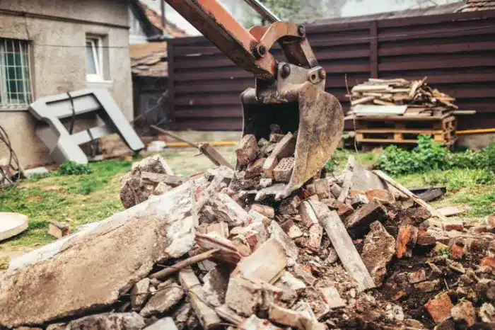 Excavator lifting debris including bricks and concrete in a residential area, illustrating debris removal services in Hagerstown, MD.