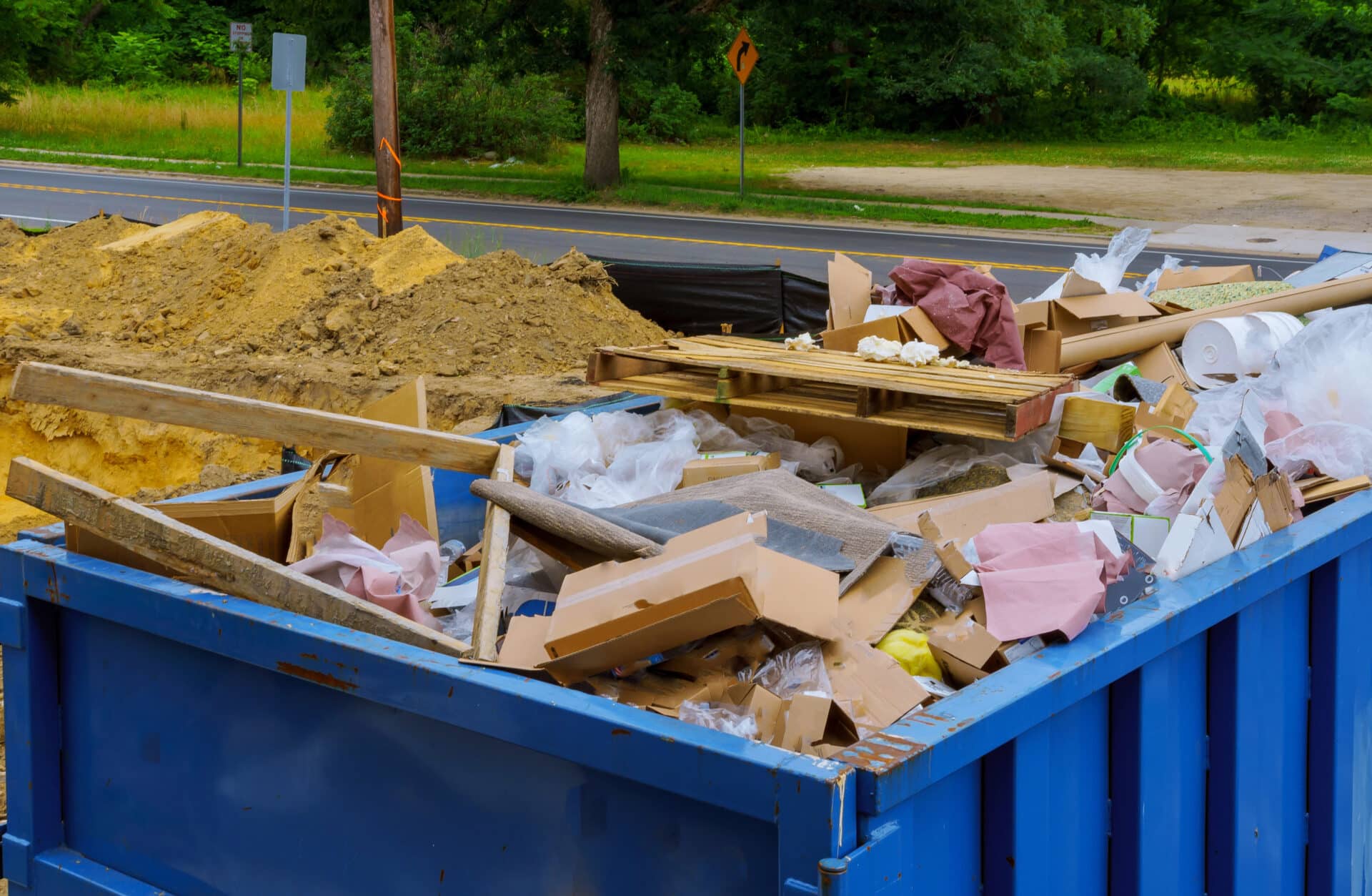 Blue dumpster filled with debris, including cardboard boxes, construction materials, and plastic waste, emphasizing the importance of junk removal in water damage cleanup.