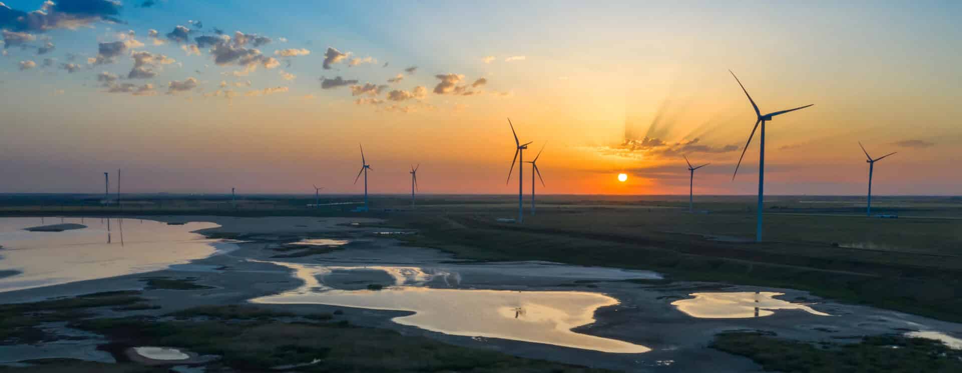 Wind turbines silhouetted against a sunset over a reflective water body, symbolizing environmental sustainability and restoration efforts.