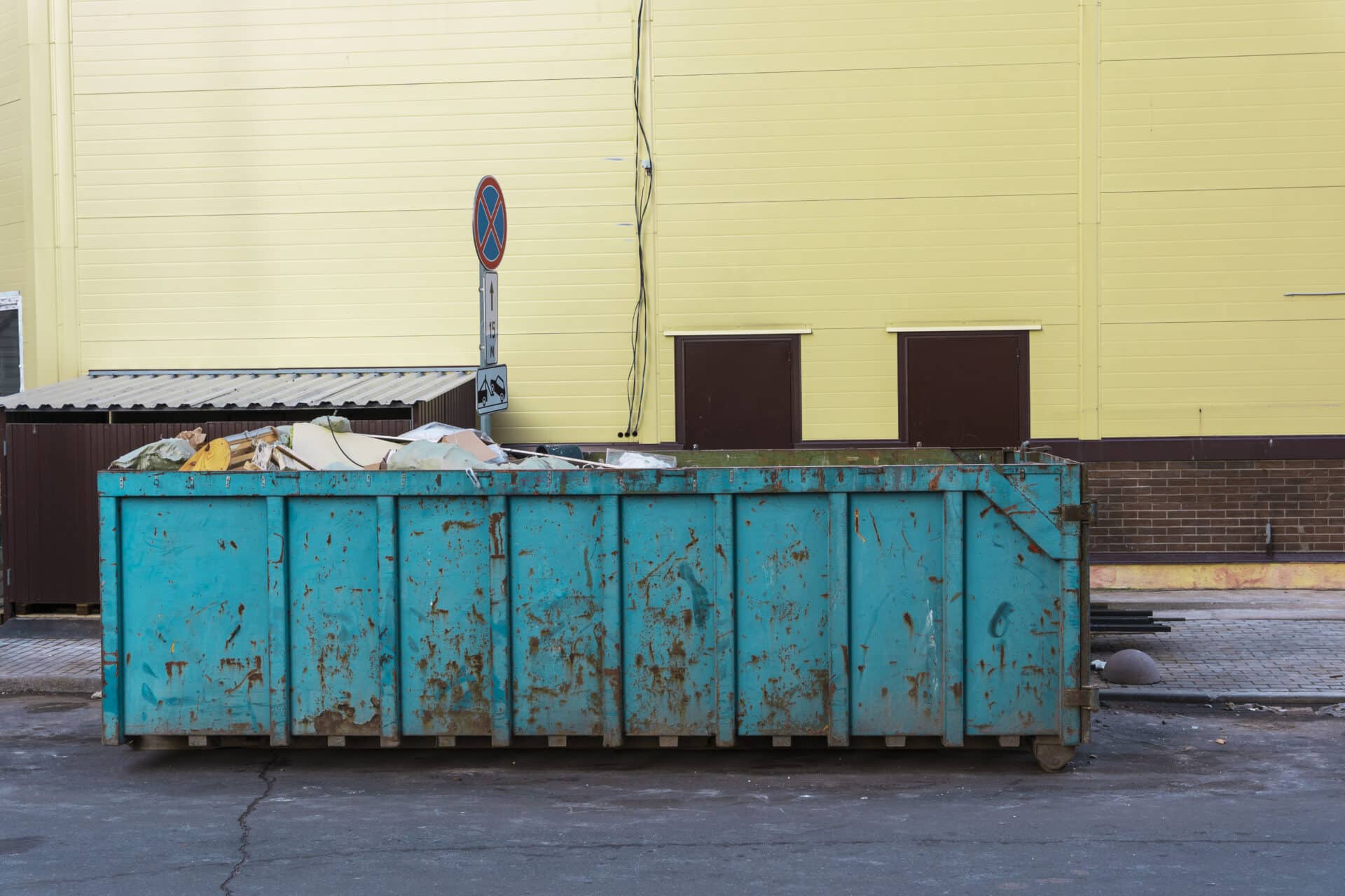 Debris-filled blue dumpster in urban setting, highlighting efficient debris removal after water damage for restoration services.