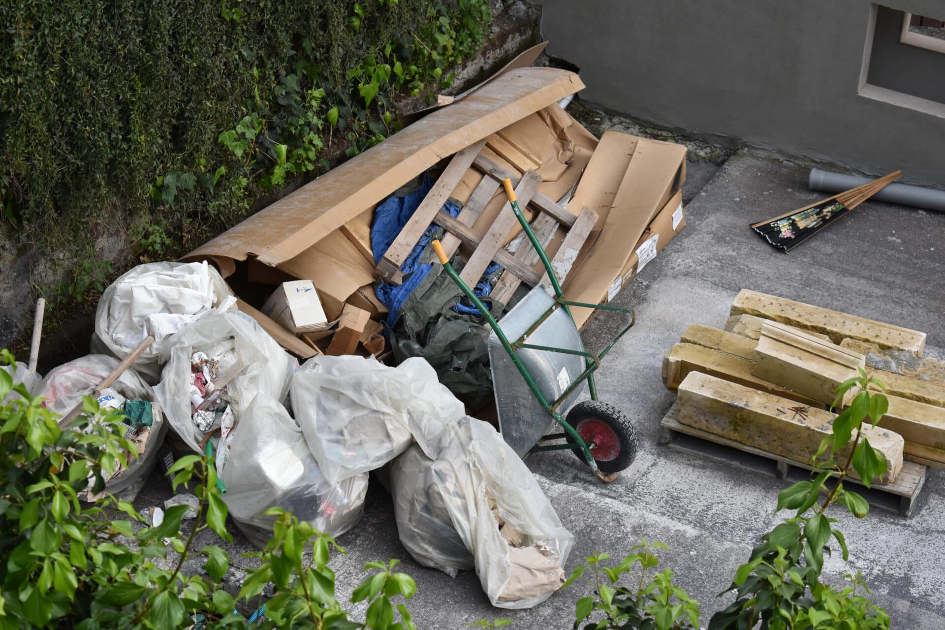 Debris piles including cardboard, bags of waste, and a wheelbarrow, illustrating the importance of junk removal for effective water damage restoration.